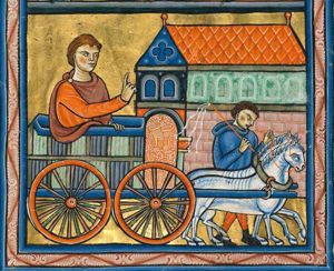 Joseph in a wagon drawn by two horses, led by a footman/crier with a whip, stretches his right hand forward in a gesture of speech; they pass a silo filled with corn.